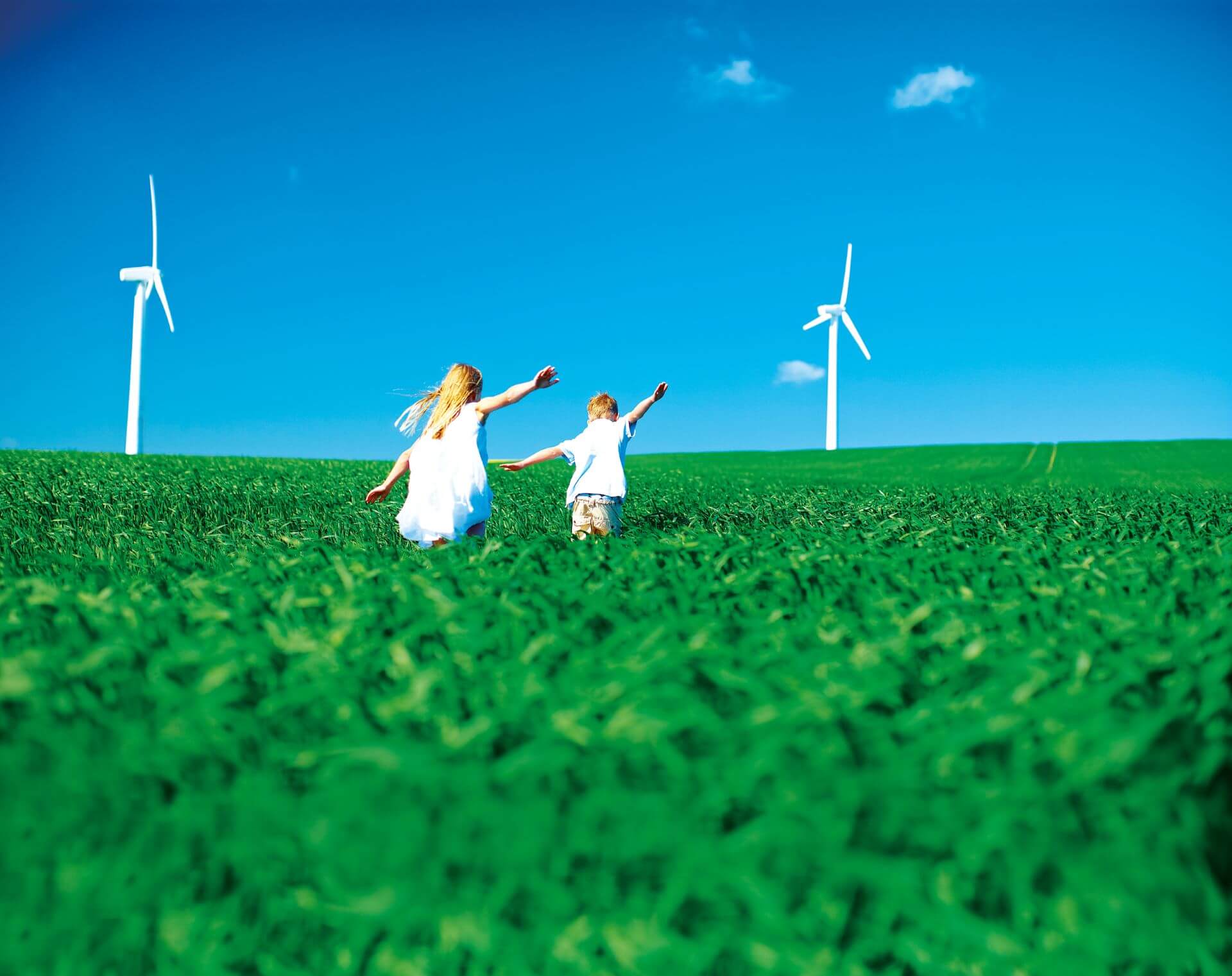 A boy and girl running on a green field with windmills