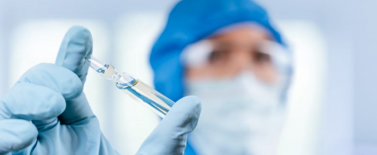 A doctor in a coverall holding a vaccine in his hands