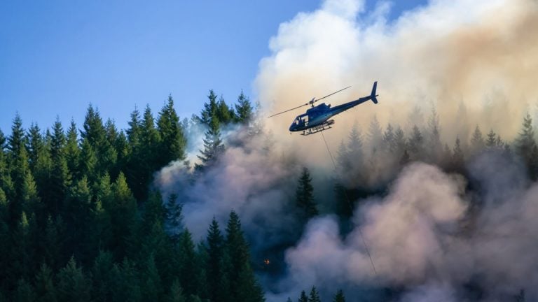 A helicopter flying in smoke over the burning forest