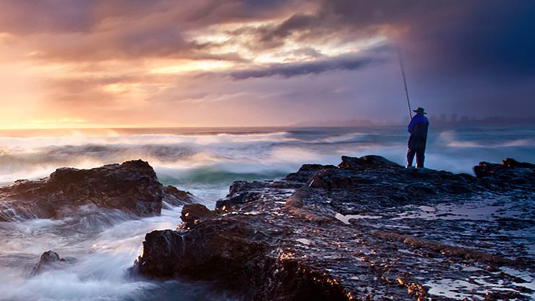 A fisherman stands on the rocks by the sea during a storm