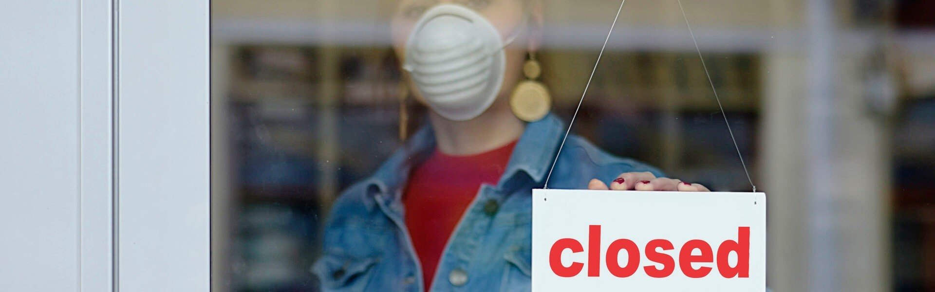 A woman in a protective mask holds the inscription "closed" in her hand