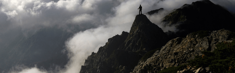 A man on a mountain top surrounded by clouds