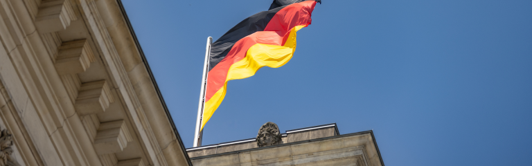 Photo of German flag fluttering above government buildings in Berlin with blue sky