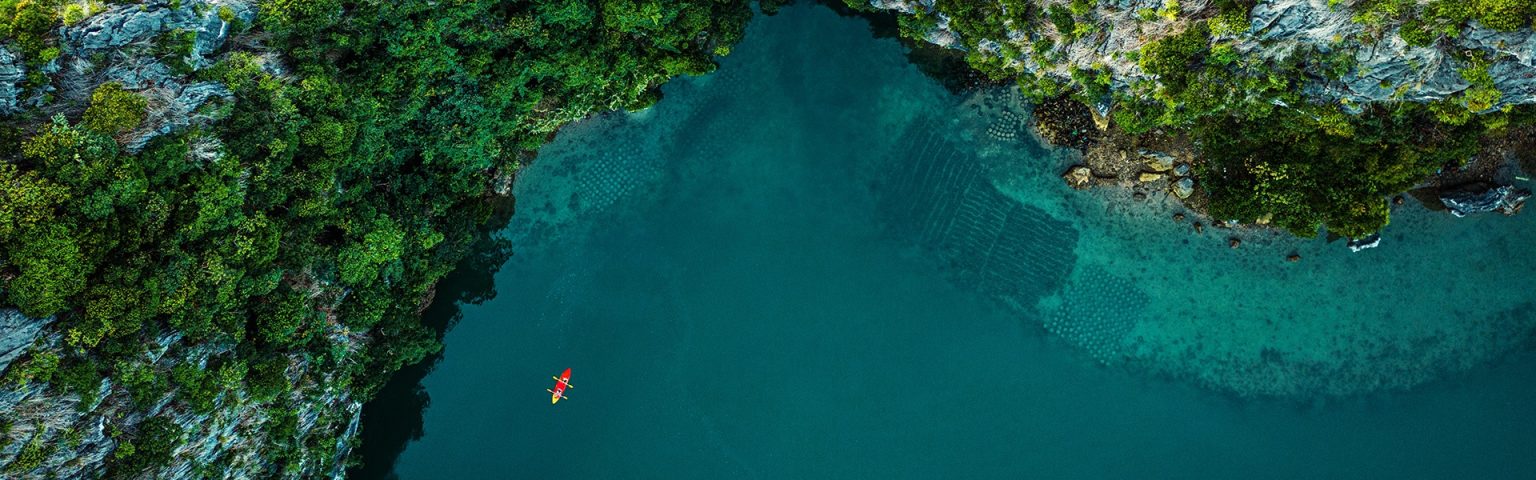 Overhead view of red kayak by rocky coastline, with deep blue sea