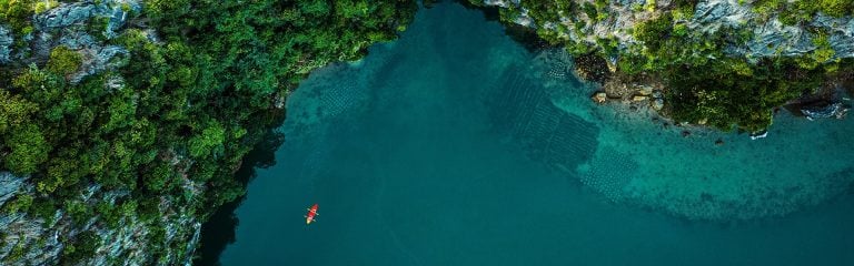 Overhead view of red kayak by rocky coastline, with deep blue sea