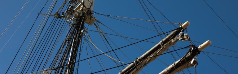 Close-up view of the intricate rigging and towering masts of a historic tall ship against a vibrant blue sky