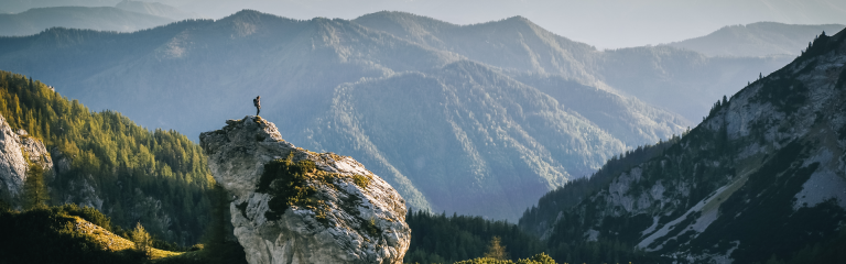 a hiker stands on top of a rock looking out over a mountain range