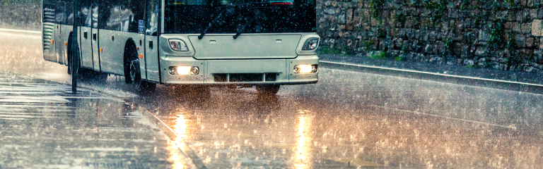 Lower half of a bus driving down a road on a rainy day