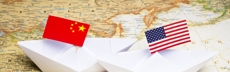 Two paper boats on top of a map of Asia, with the US and China flags on each, respectively.