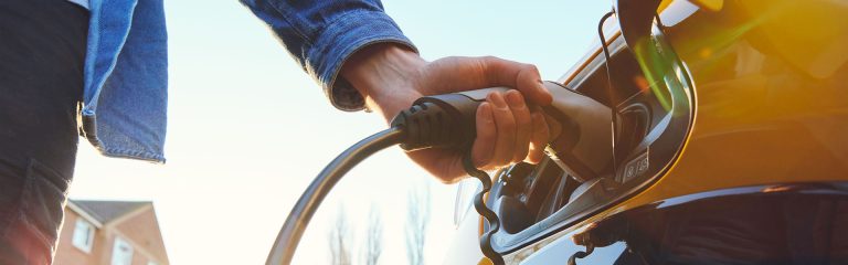 A motorist charges a yellow electric vehicle using a large plug.