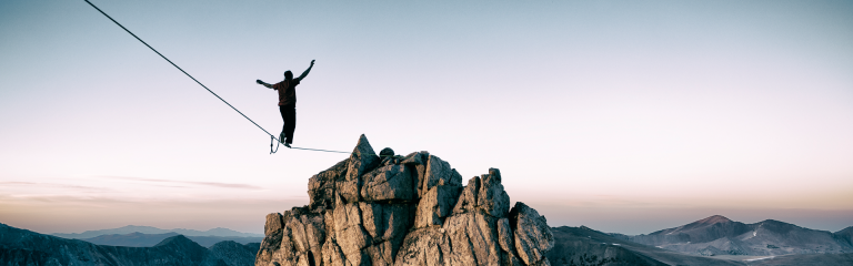 a person is balancing on a wire that leads to a rocky outcrop