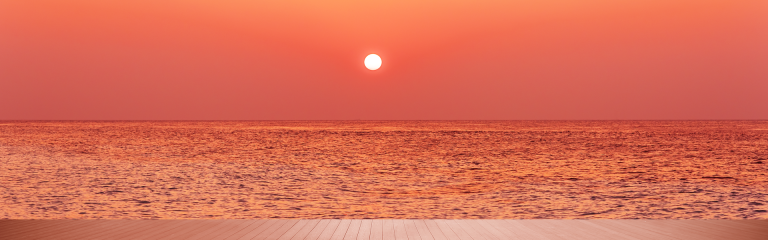 a setting sun in a central position against a red sky with a wooden deck in view at the base.