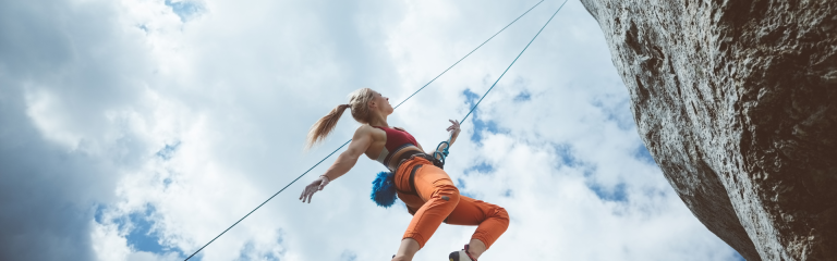 a woman is rock climbing. She is suspended by a rope from a cliff face