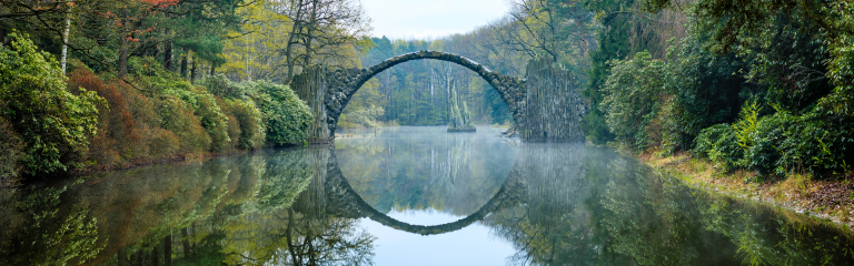 Arched stone bridge over a still, misty lake, surrounded by forest