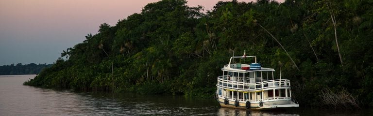 A white ferry boat travels down the Amazon river at dusk.