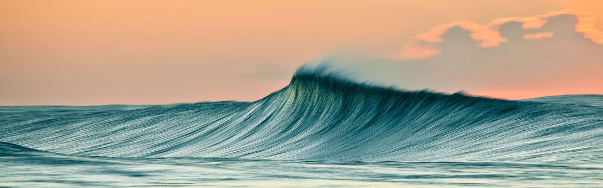 Offshore wind picking up a peaking wave in the early light of sunrise