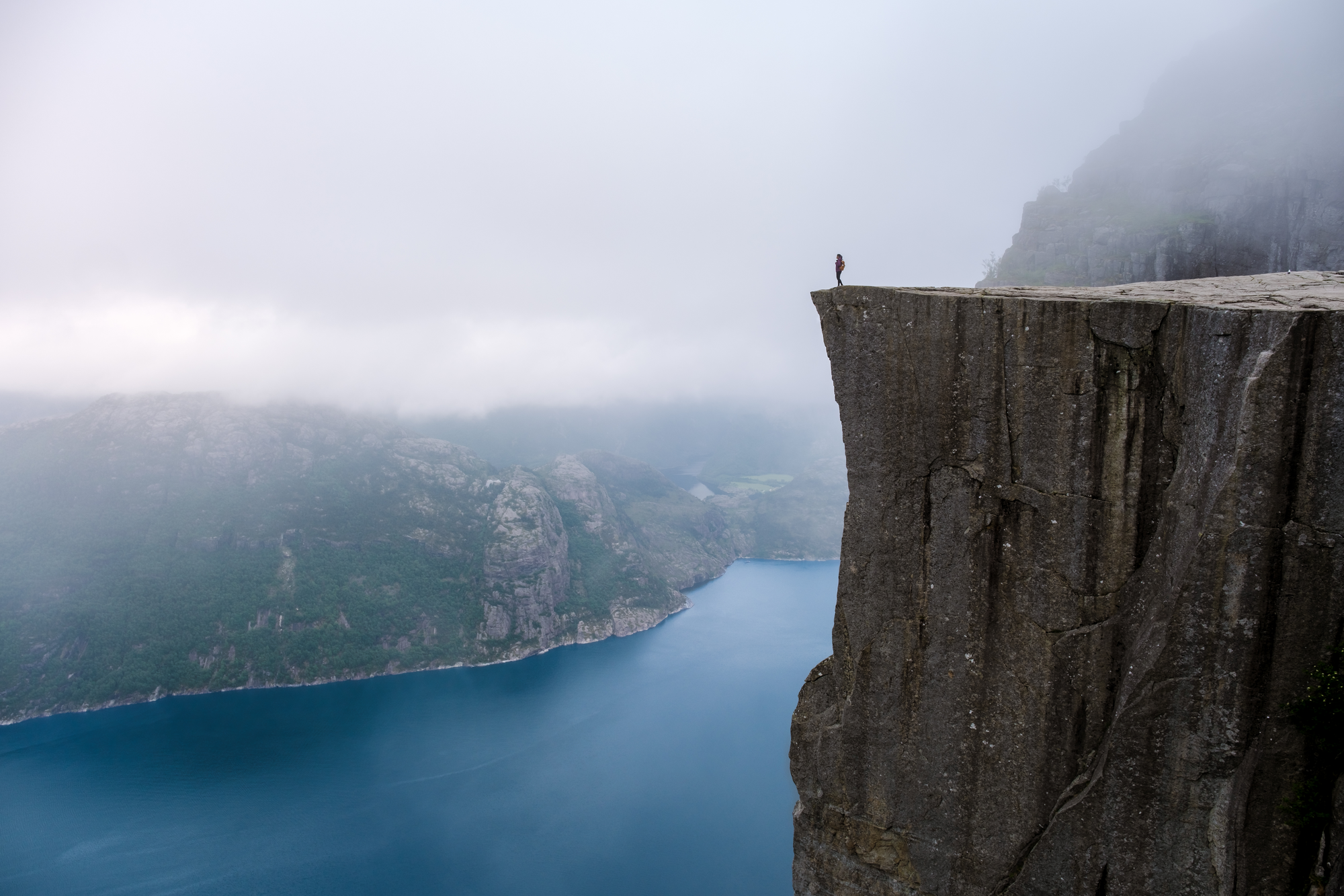 a man stands on the cliff edge in Norway overlooking the water.