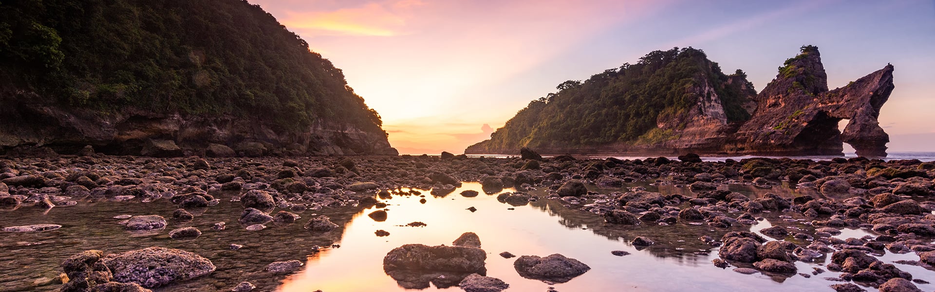 Sunrise over a rocky bay, with light glancing off the water in the foreground.