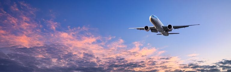 Commercial airplane taking off against the backdrop of a blue sky with rose-tinted clouds