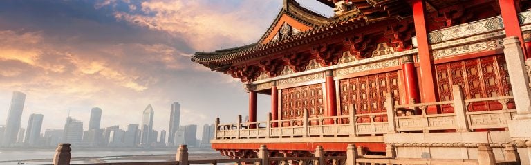 Red and gold traditional Asian temple in right foreground with modern city skyline across the harbour beyond