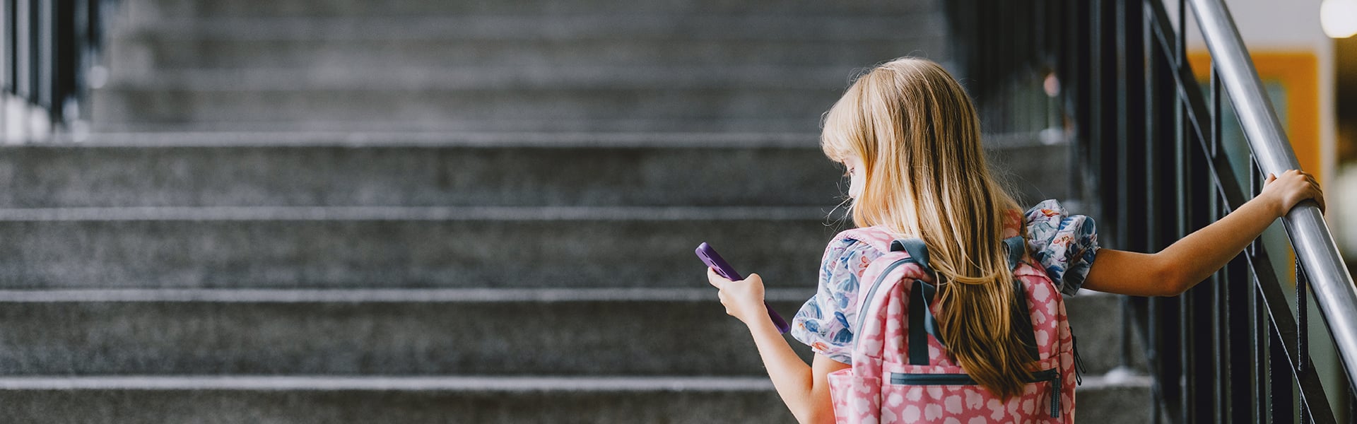 Young girl with school backpack looks at phone as she prepares to climb staircase