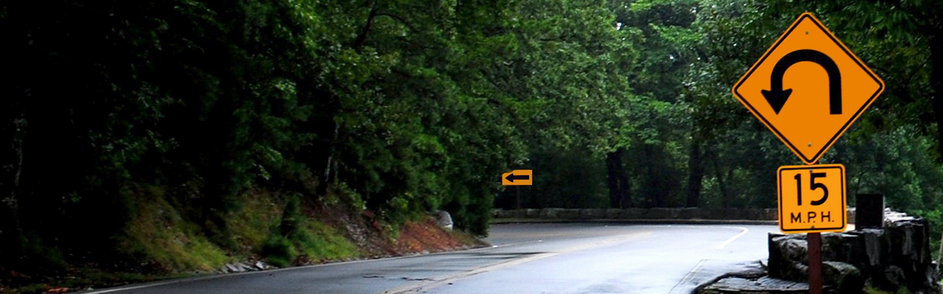 U-turn sign next to a bend in the road, surrounded by trees