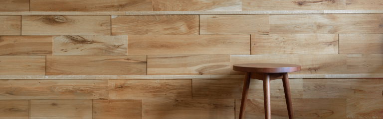 three-legged wooden stool propped up against a wood-panelled wall